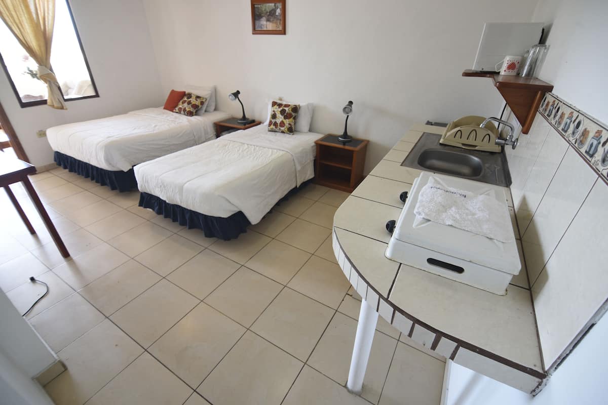 A hotel room with two beds, a small sink, and a mirror.