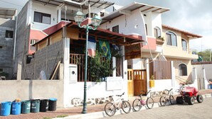 A two-story building with a balcony, a bicycle, and a red vehicle parked outside. - Galapagos Best Hostel (Puerto Ayora)