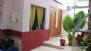 A building with a red and white facade, wooden doors, and a small porch area with potted plants. - Galapagos Best Hostel (Puerto Ayora)
