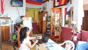 A room with a laptop on a table, a television on the wall, and various items on shelves and a cabinet. - Galapagos Best Hostel (Puerto Ayora)