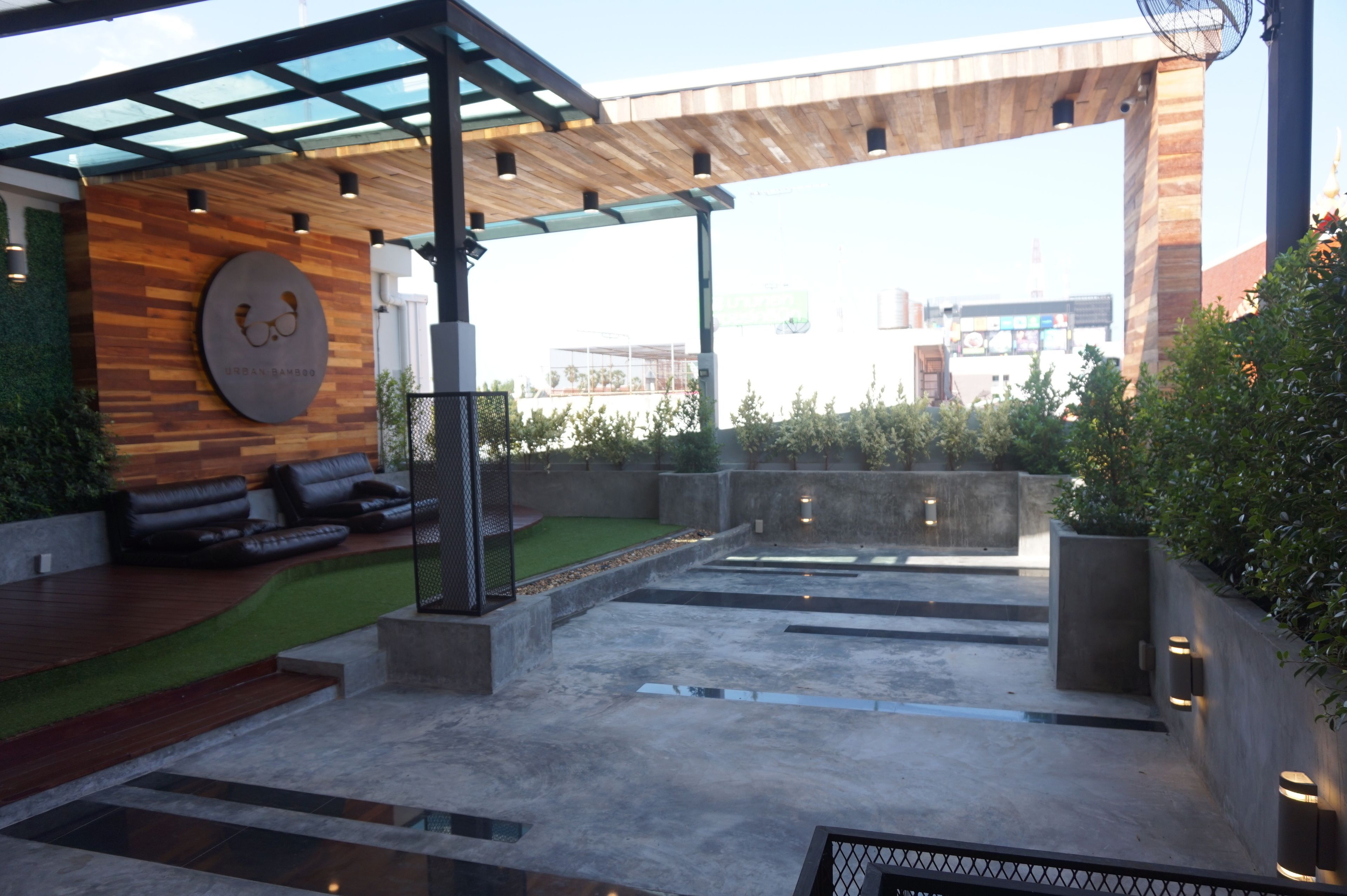 A modern outdoor seating area with a wooden wall, a glass canopy, and a view of the cityscape.
