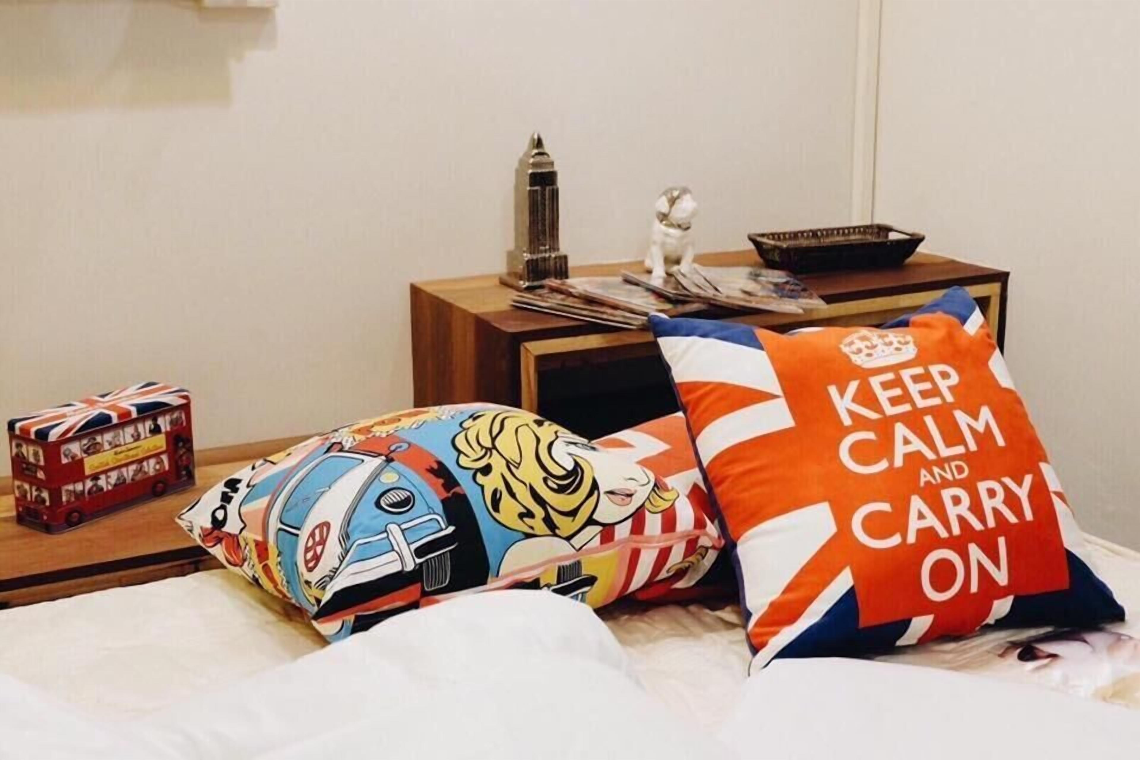 A bed with colorful pillows, a small table with a lamp, a decorative item, and a toy bus.
