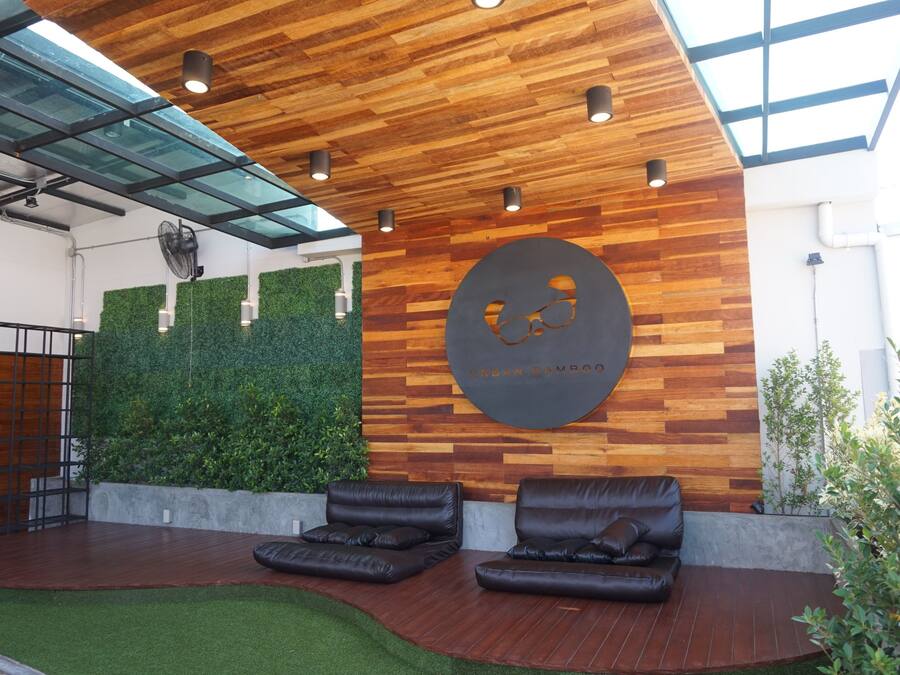 A modern lobby with wooden ceiling panels, a glass roof, and a green wall with a circular logo. There are two leather sofas and a small staircase.