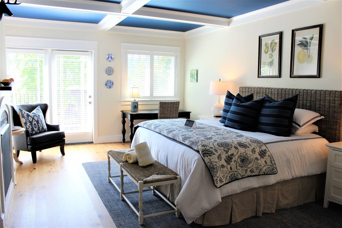 A bedroom with a large bed, a bench, a chair, a nightstand, and a desk.