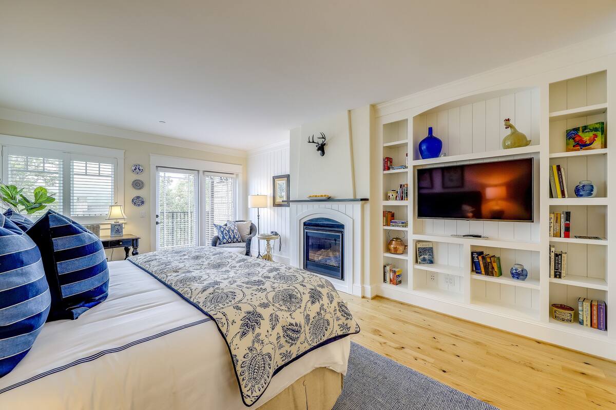 A well-lit room with a bed, a fireplace, and a TV on a white entertainment unit.