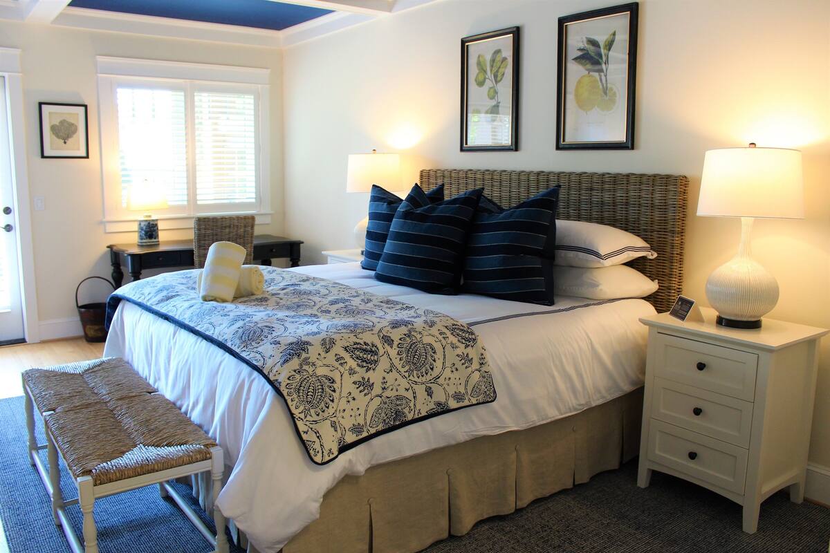 A bedroom with a bed, bedside tables, a bench, and a window with blinds.