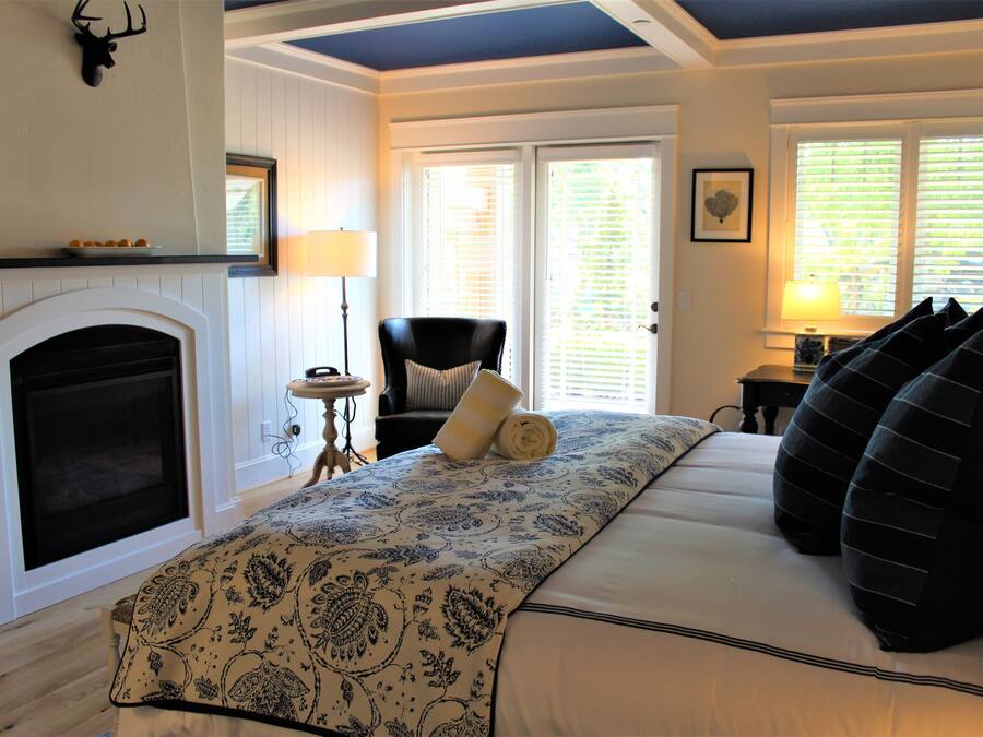 Une chambre avec une cheminée, un lit avec une literie à motifs, une chaise et une lampe.