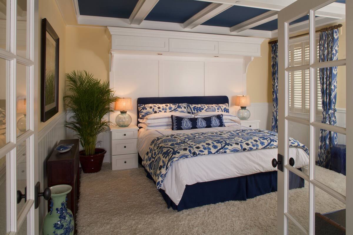 A bedroom with a bed, bedside tables, a potted plant, and a door.