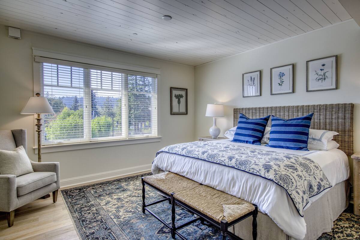 A bedroom with a large bed, a bench, a chair, and a window with blinds.