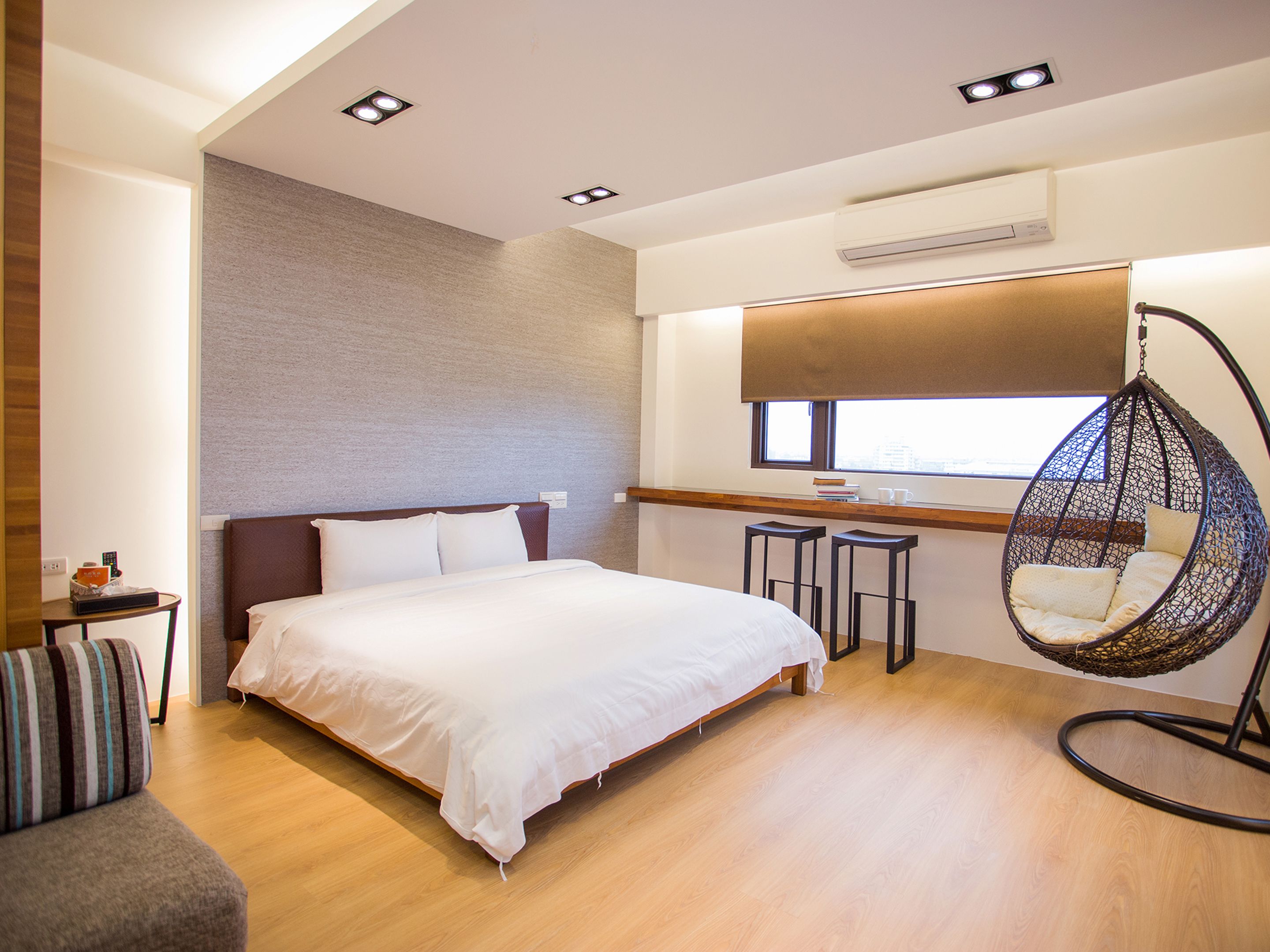 Quarto de hotel moderno com uma cama grande, uma cadeira suspensa e uma pequena mesa com bancos.