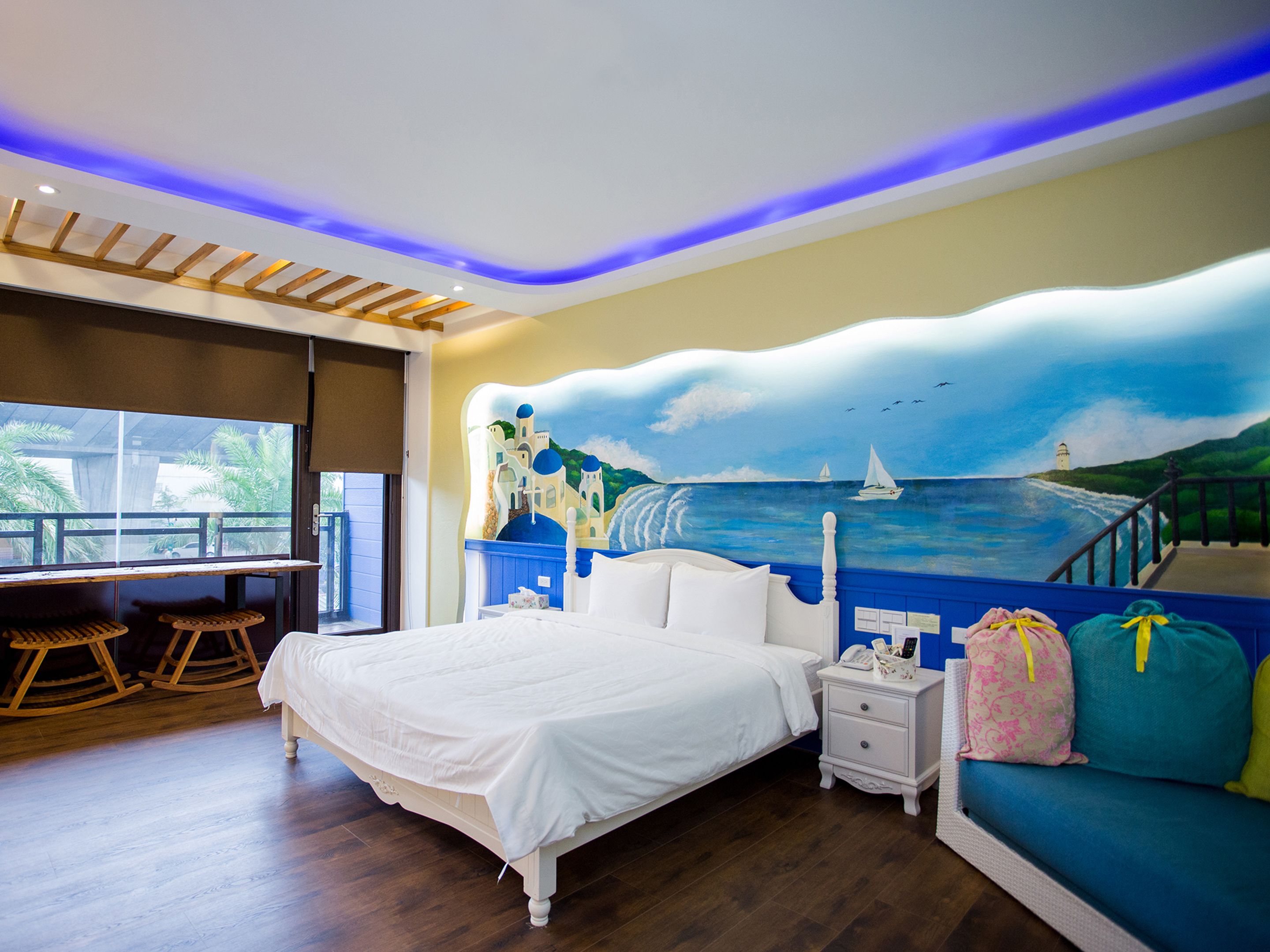 Une chambre à coucher comprenant un lit, une table de chevet, un fauteuil à bascule, une fenêtre avec vue et une fresque murale.