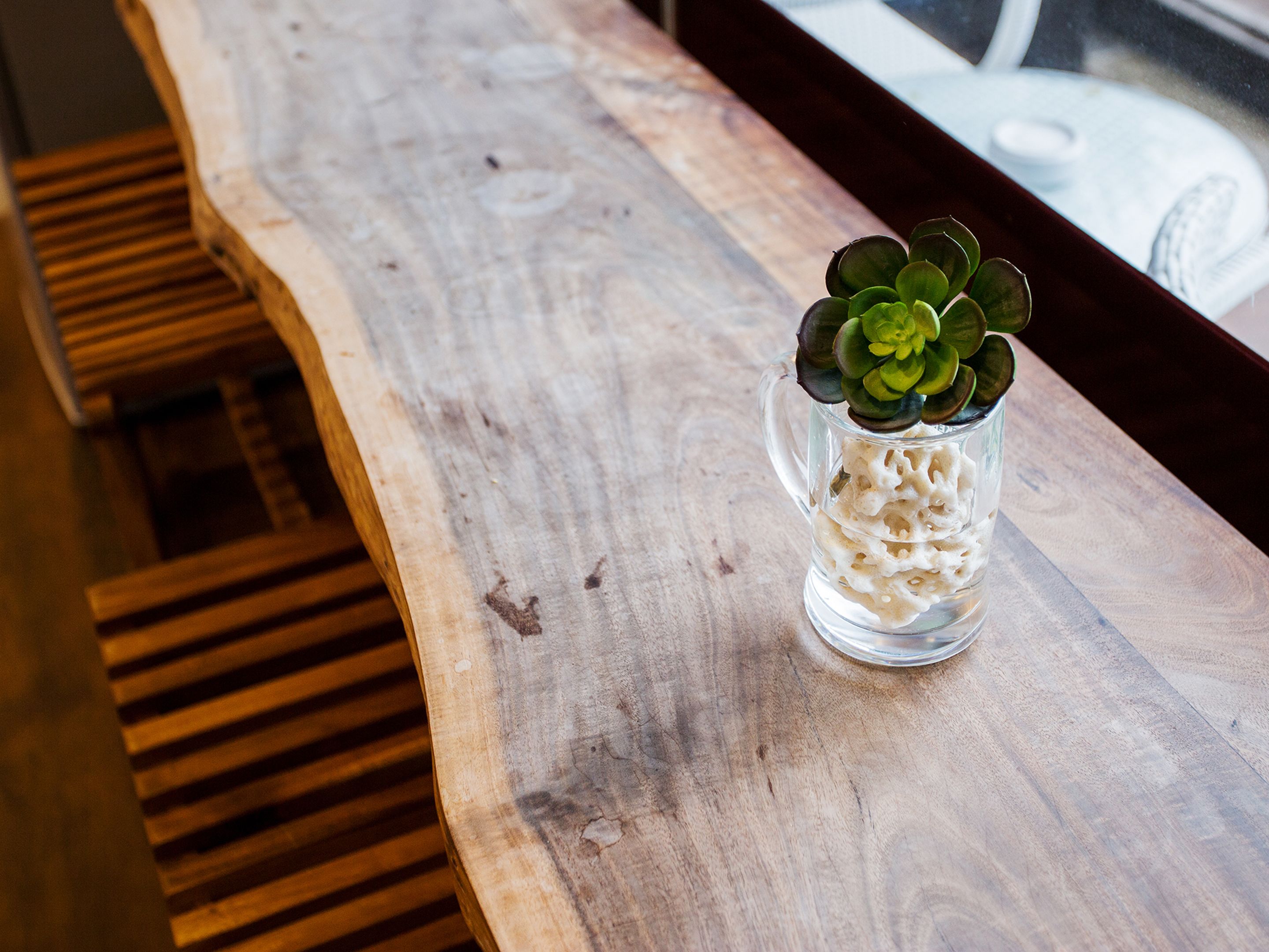 A wooden bench with a glass vase containing a succulent plant.