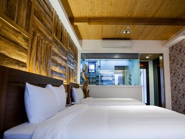 Habitación de hotel con cabecera de madera, dos camas con sábanas blancas, un espejo grande y vistas al baño y al pasillo.