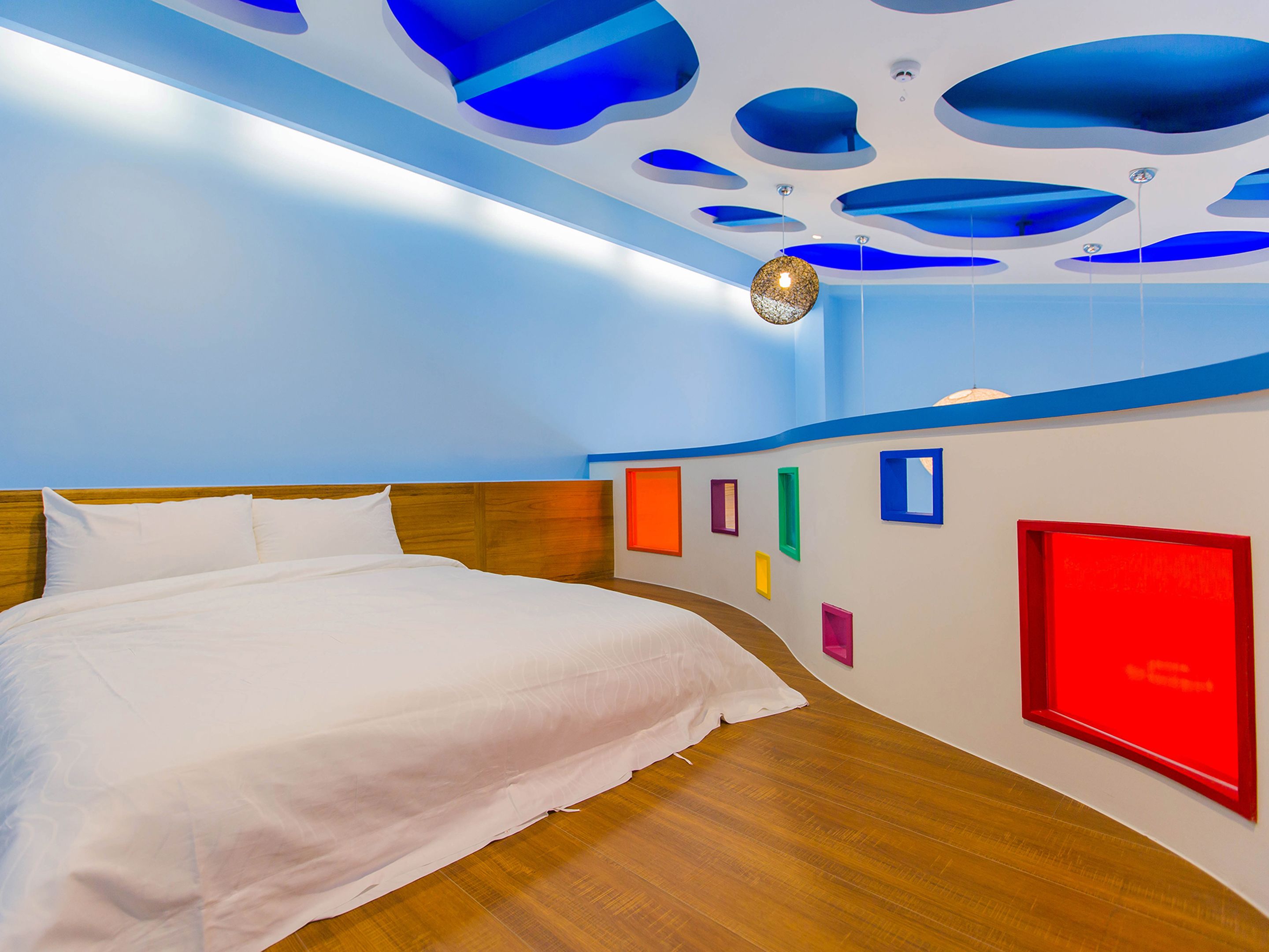 Une chambre d’hôtel moderne avec un plancher en bois, un grand lit et un plafond au design original, orné de motifs bleus et blancs.