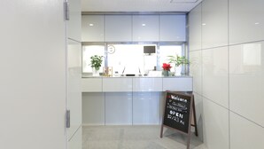 A reception area with a glass partition, a clock, a television, and a welcome sign indicating the hotel is open. - Oak Hotel Edo (Tokyo)