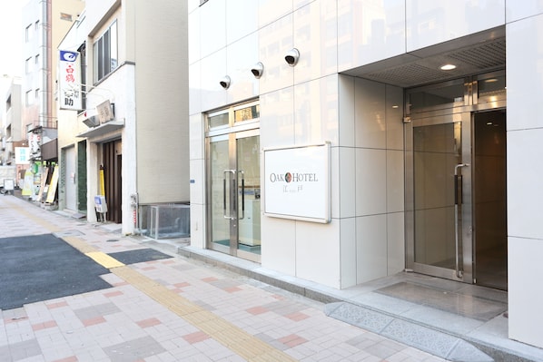 A modern hotel entrance with a glass door, a signboard, and a tiled pavement.