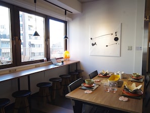 A dining area with a wooden table set for two, bar stools, a laptop, and a pendant light. - Oak Hotel Edo - Hostel (Tokyo)