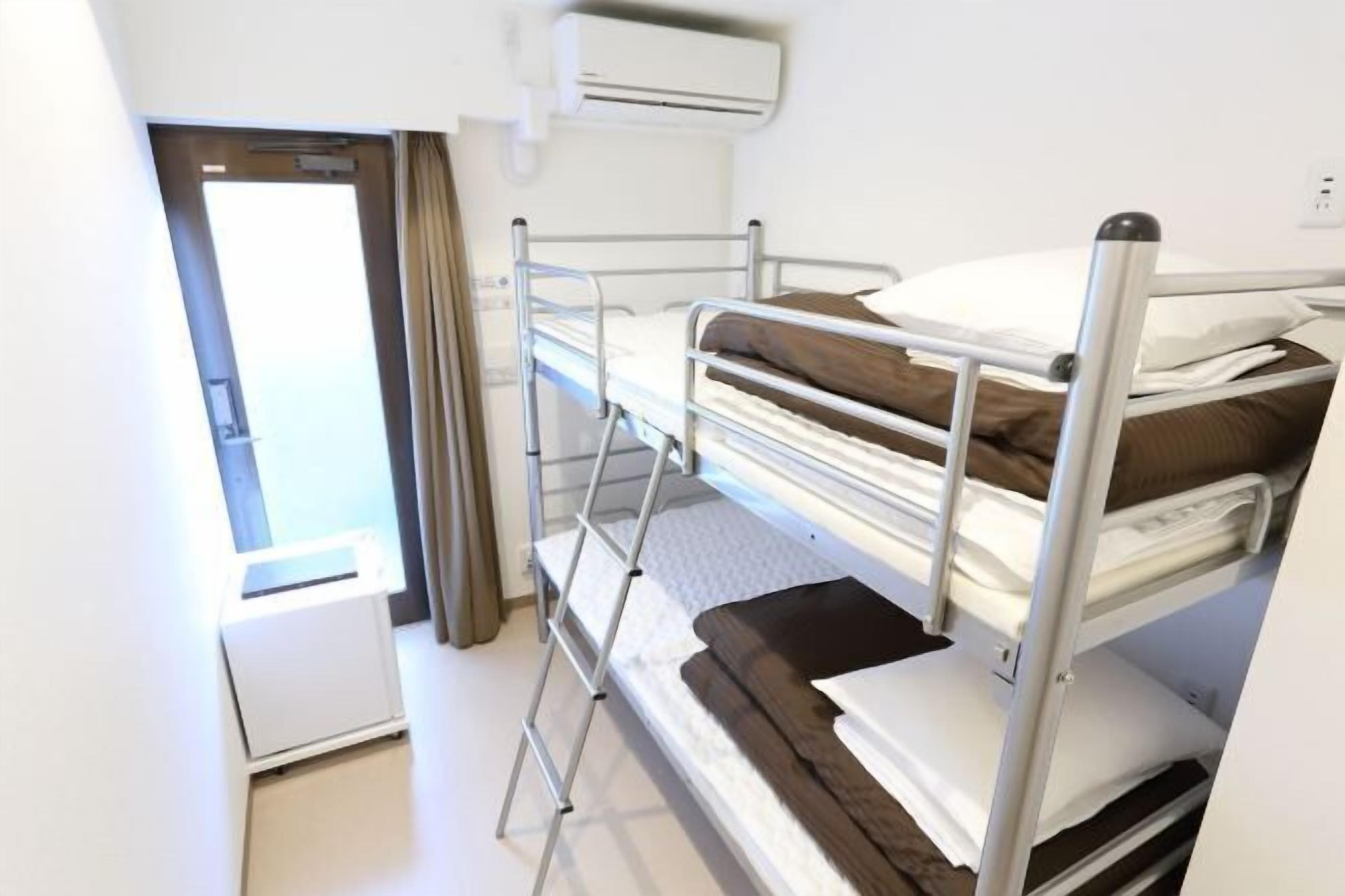 A bunk bed room with a window, a desk, and an air conditioning unit.