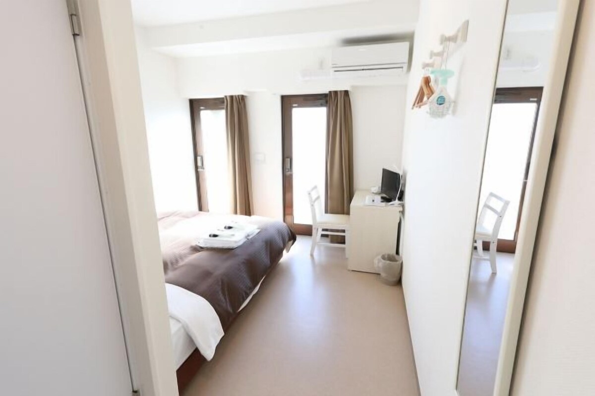 Une chambre d’hôtel avec un lit, un bureau, une chaise et un miroir.