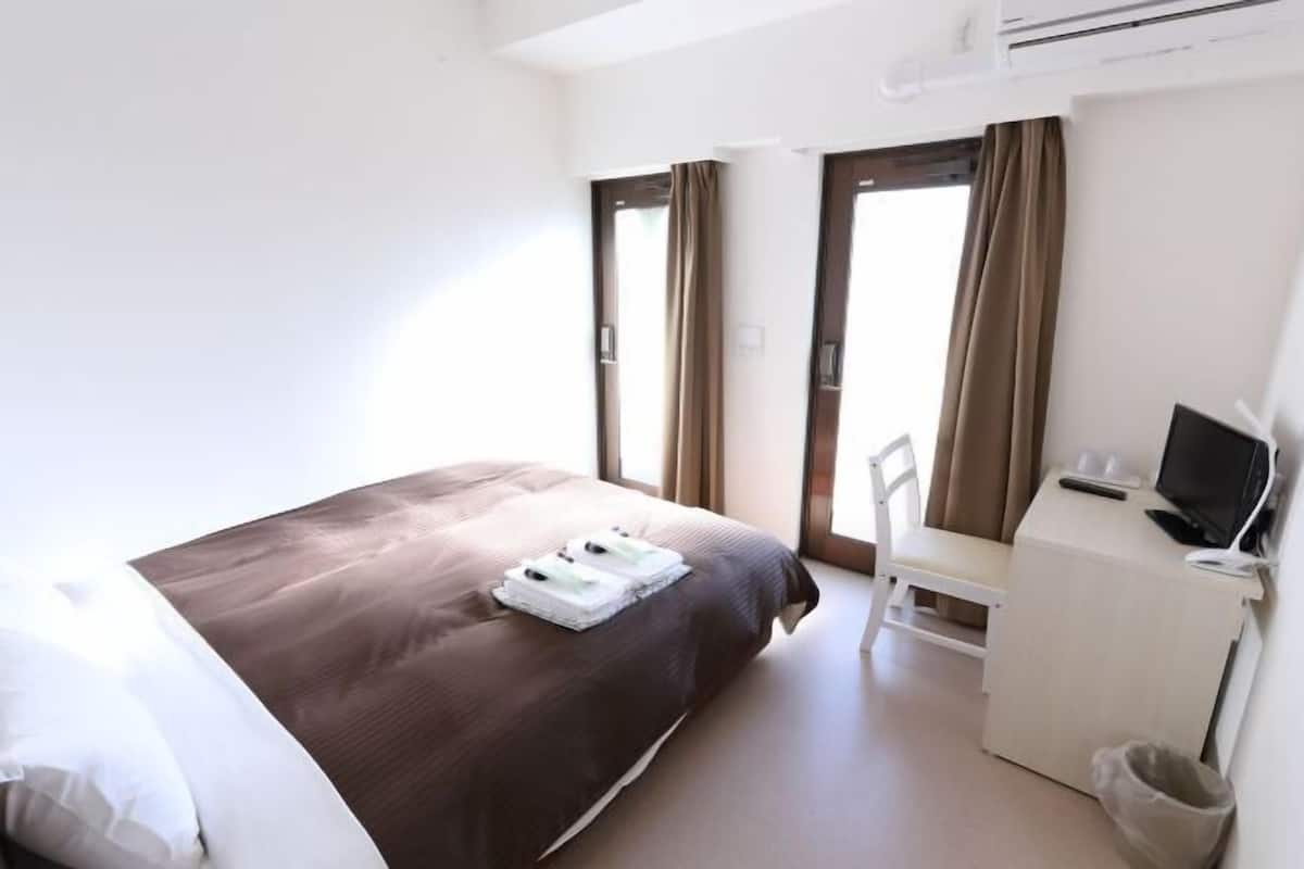 A hotel room with a bed, a desk, a chair, and a TV.