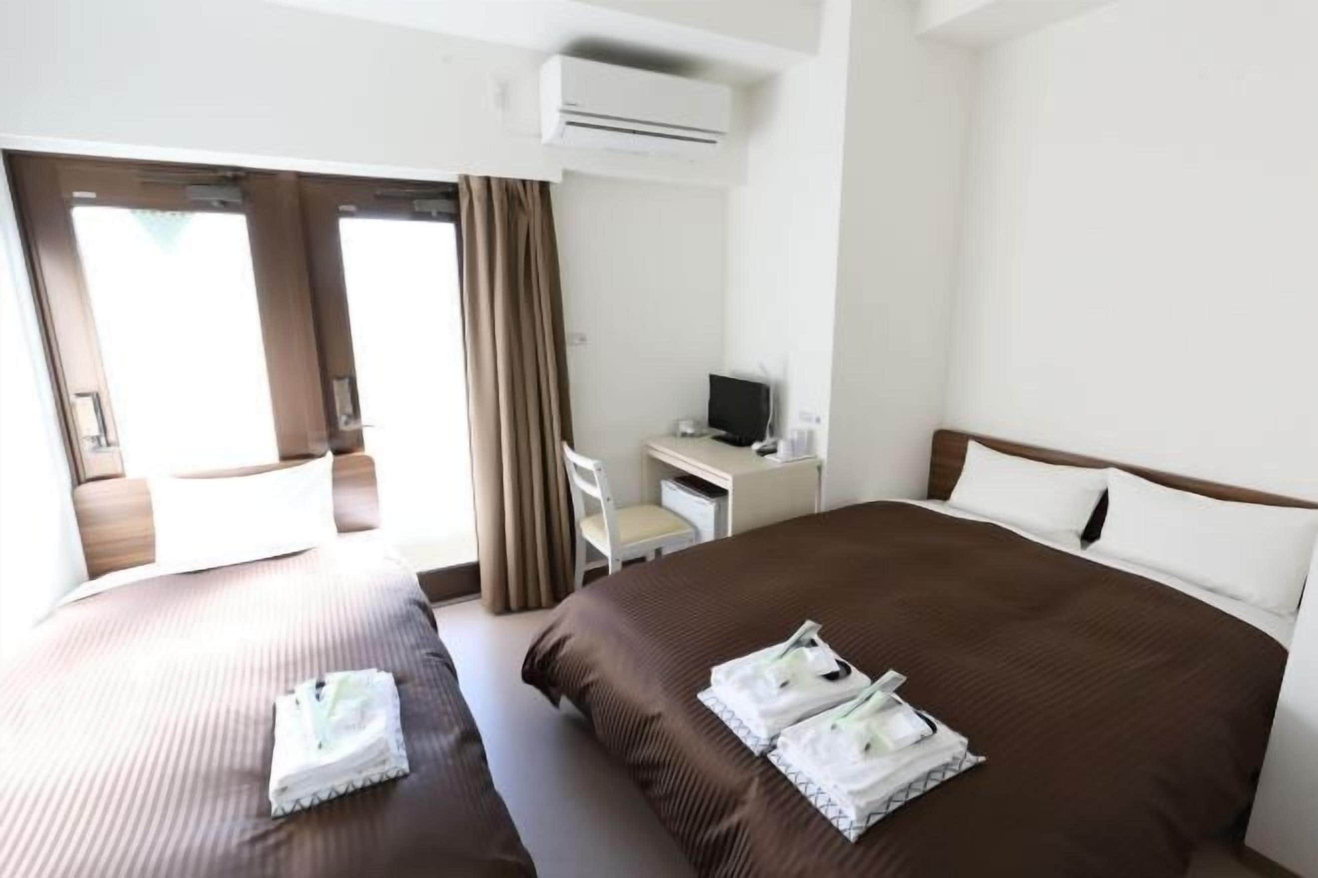 A hotel room with two beds, a desk, a chair, and an air conditioning unit.