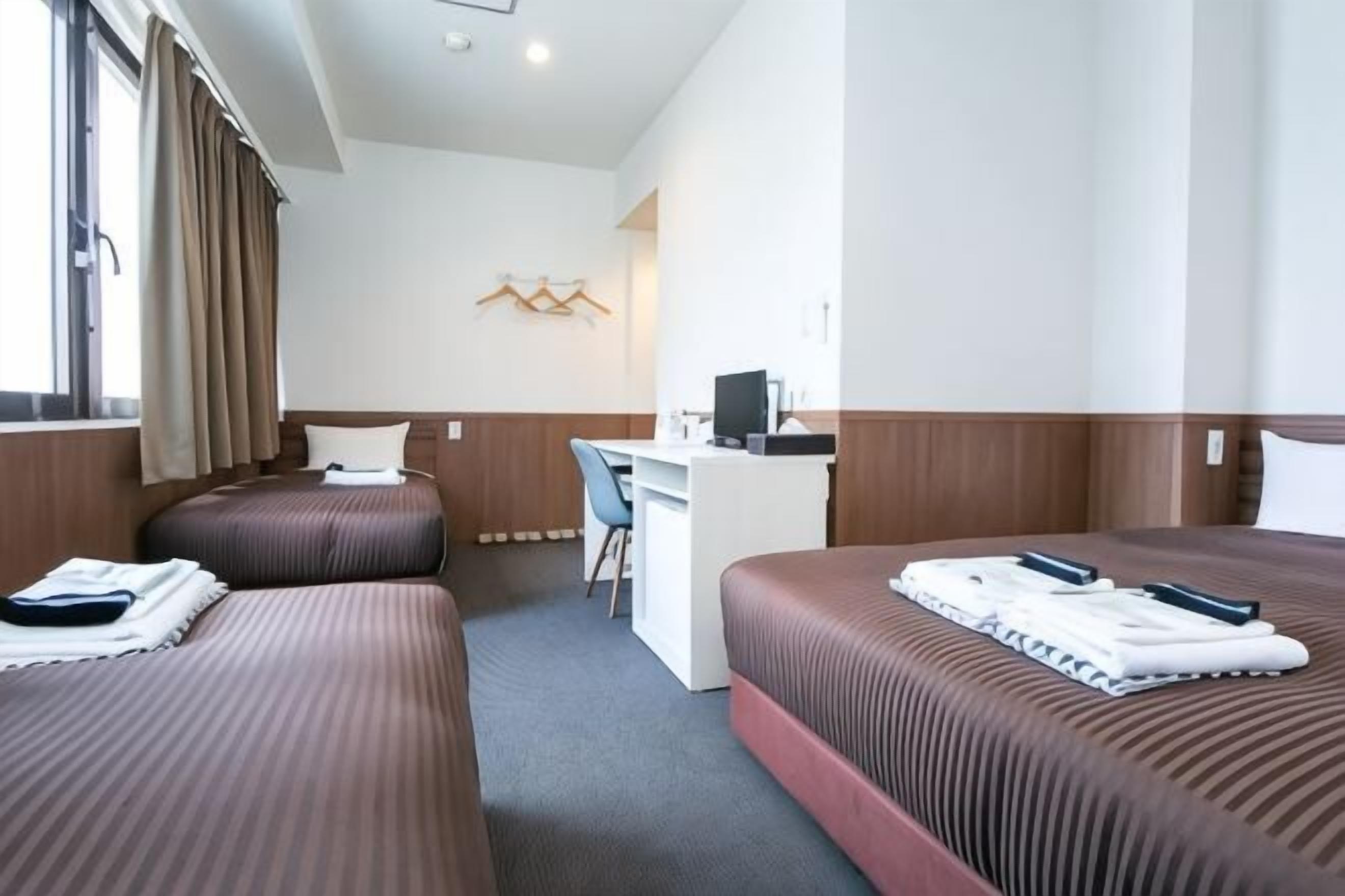 A hotel room with two beds, a desk, and a computer.