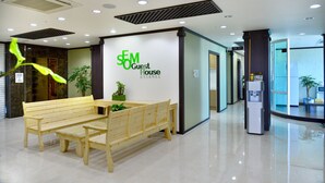 A clean, modern lobby with a wooden bench, a reception desk, and a sign for the guest house. - Seom Guesthouse - Hostel (Seogwipo)