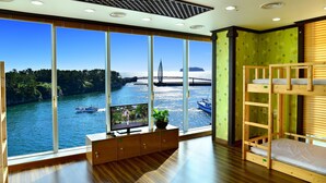 A room with large windows overlooking a river, a bunk bed, and a wooden cabinet with a plant. - Seom Guesthouse - Hostel (Seogwipo)