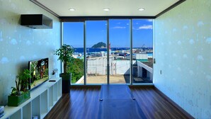 A modern hotel room with a large sliding glass door leading to a balcony with a view of the sea and a distant island. - Seom Guesthouse - Hostel (Seogwipo)