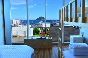 Habitación de hotel con una ventana grande, suelo de madera, cama, televisión y una pequeña kitchenette.