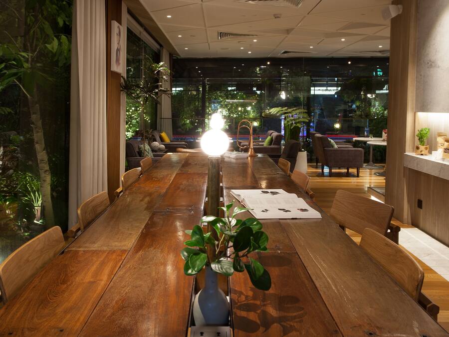A long wooden table with chairs, a vase with plants, and a bright light in the center.