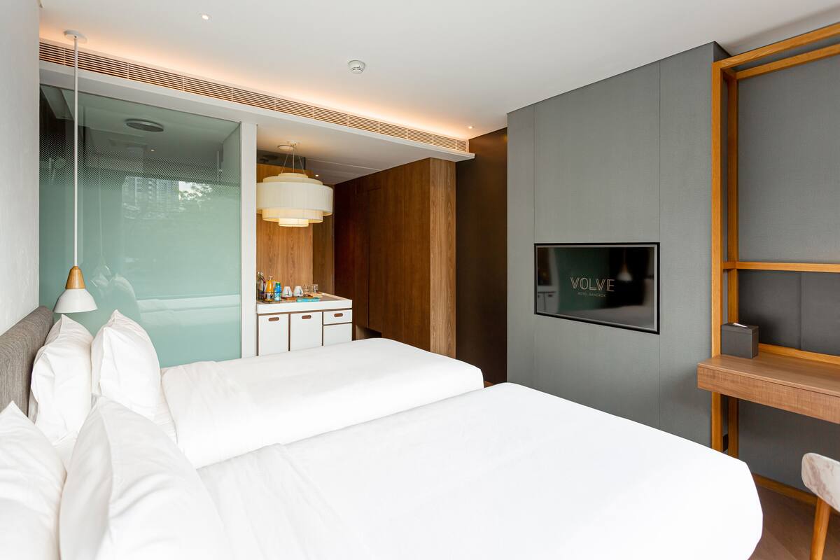 A modern hotel room with a large bed, a vanity with a mirror, and a television mounted on the wall.