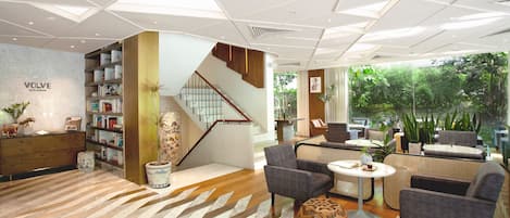 Un vestíbulo de hotel moderno con un suelo de diseño en espiga, una escalera y una zona de estar con sofás y una mesa de centro.