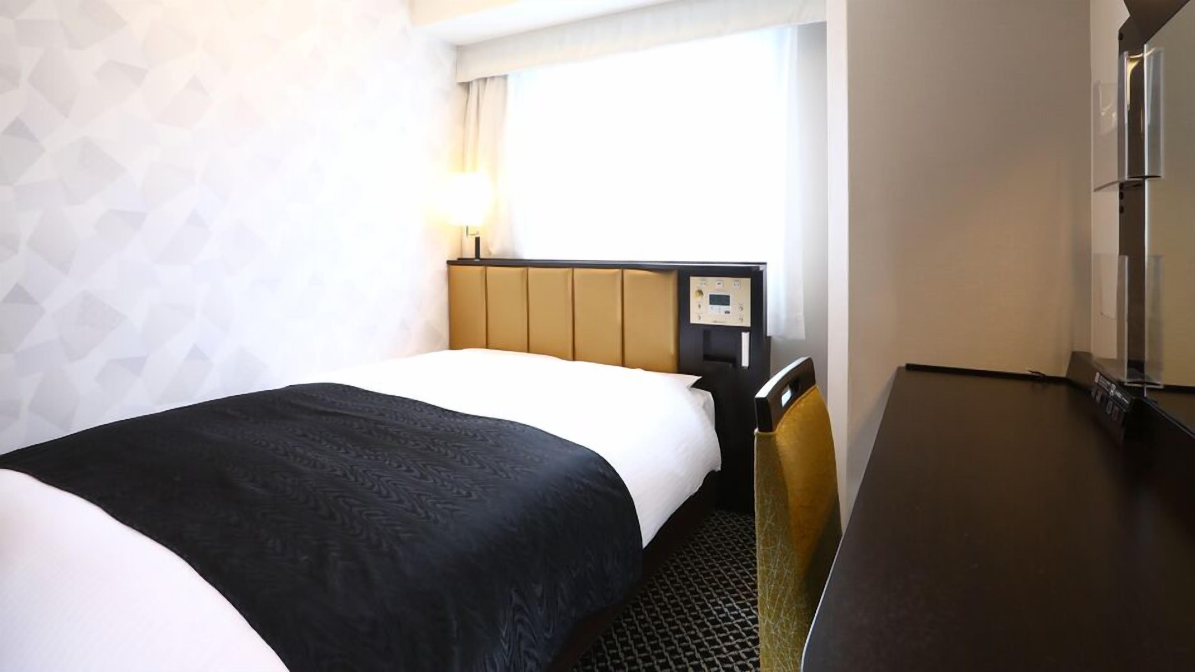 A hotel room with a bed, a desk, and a window.