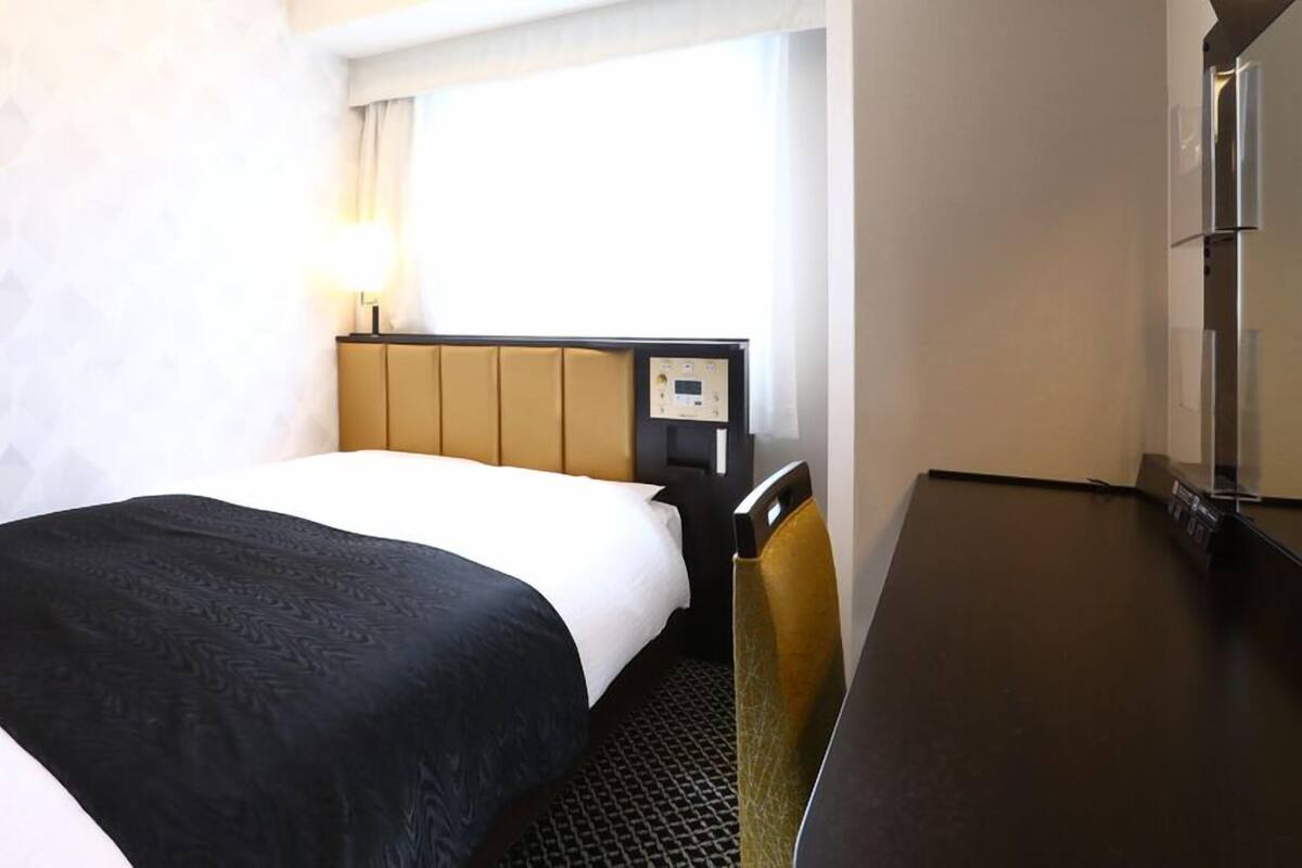 Quarto de hotel com uma cama, uma escrivaninha e uma janela.
