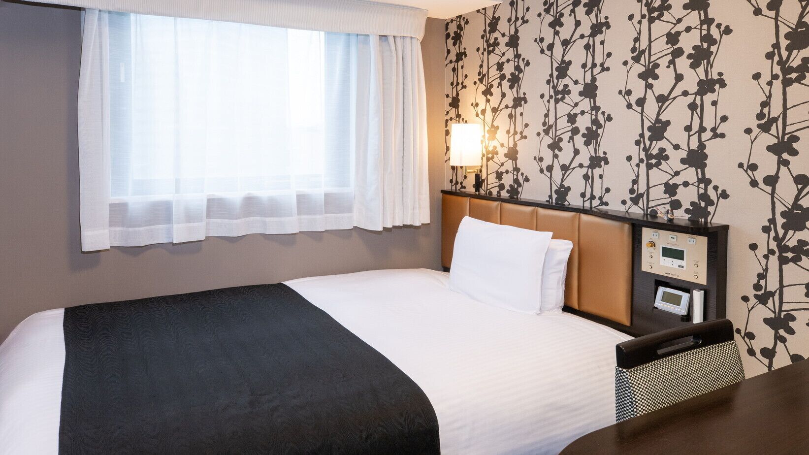 A hotel room with a bed, a bedside table, a lamp, and a control panel.