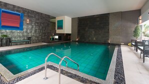 Ein Schwimmbecken mit Fliesenboden, Metallhandläufen und einer Sitzgruppe mit Bänken.