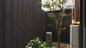 Un petit espace extérieur, délimité par une clôture en bois, avec un jeune arbre, une lanterne en pierre et un réfrigérateur.