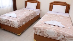 Two twin beds with brown headboards and white bedding, a white towel on each bed, and a 'KOPEN' brand tag on the beds. - DeKopen Rooms & Convention (Malang)