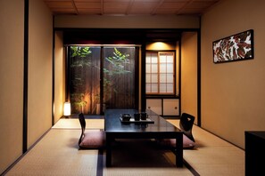 A traditional Japanese room with tatami flooring, a low table with a tray, two chairs, and a sliding door with a view of greenery. - Rinn Kujoharikoji 59 (Kyoto)