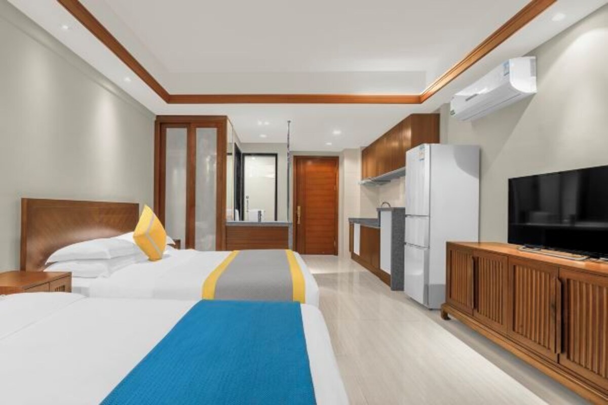 A hotel room with two beds, a kitchenette, a TV, and a wooden cabinet.