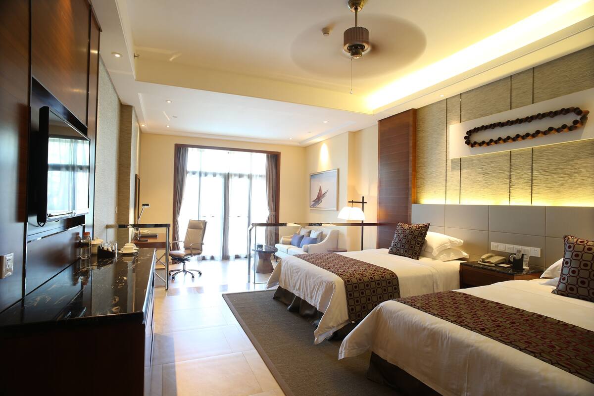 A hotel room with two beds, a desk, a chair, and a TV.