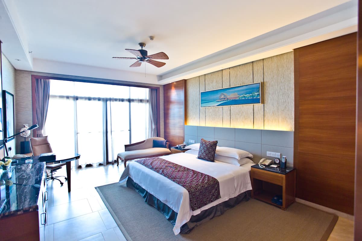 A hotel room with a large bed, a desk, a chair, a nightstand, and a ceiling fan.