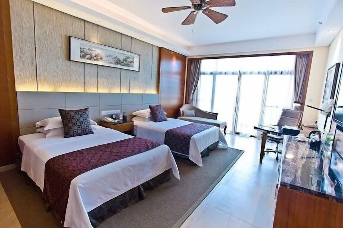 A hotel room with two beds, a desk, a chair, a television, and a large window.