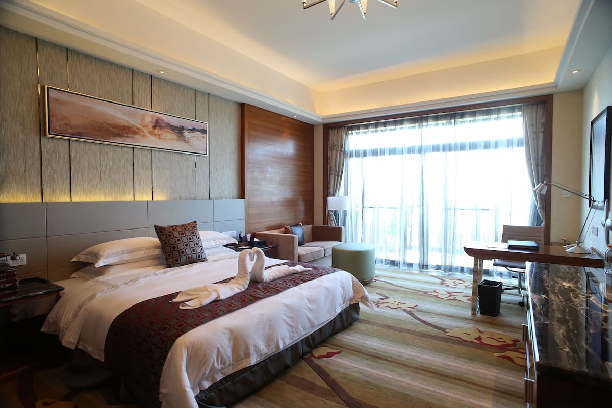 A hotel room with a large bed, a desk, a chair, and a TV.