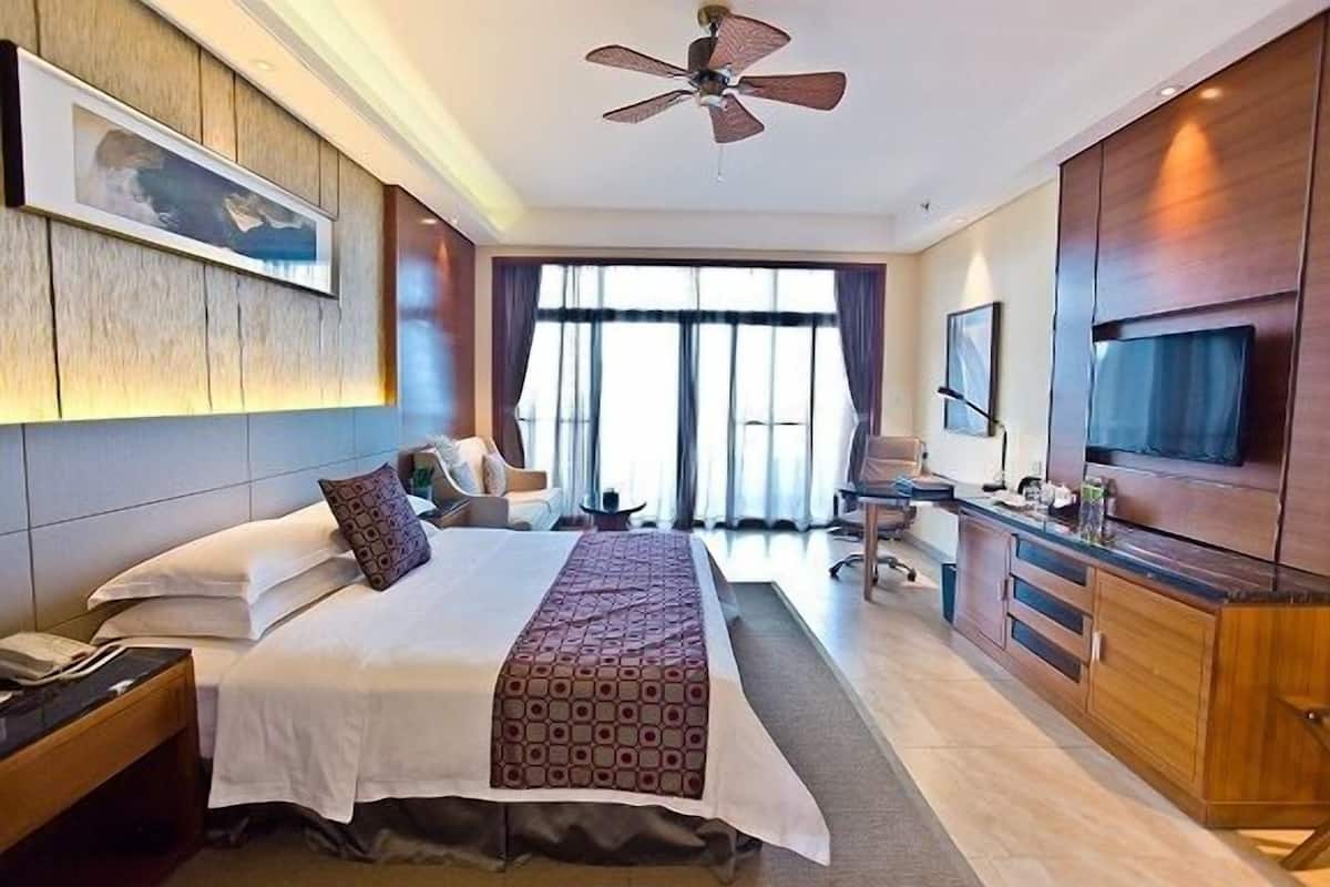 A hotel room with a large bed, a desk with a chair, a television, and a ceiling fan.