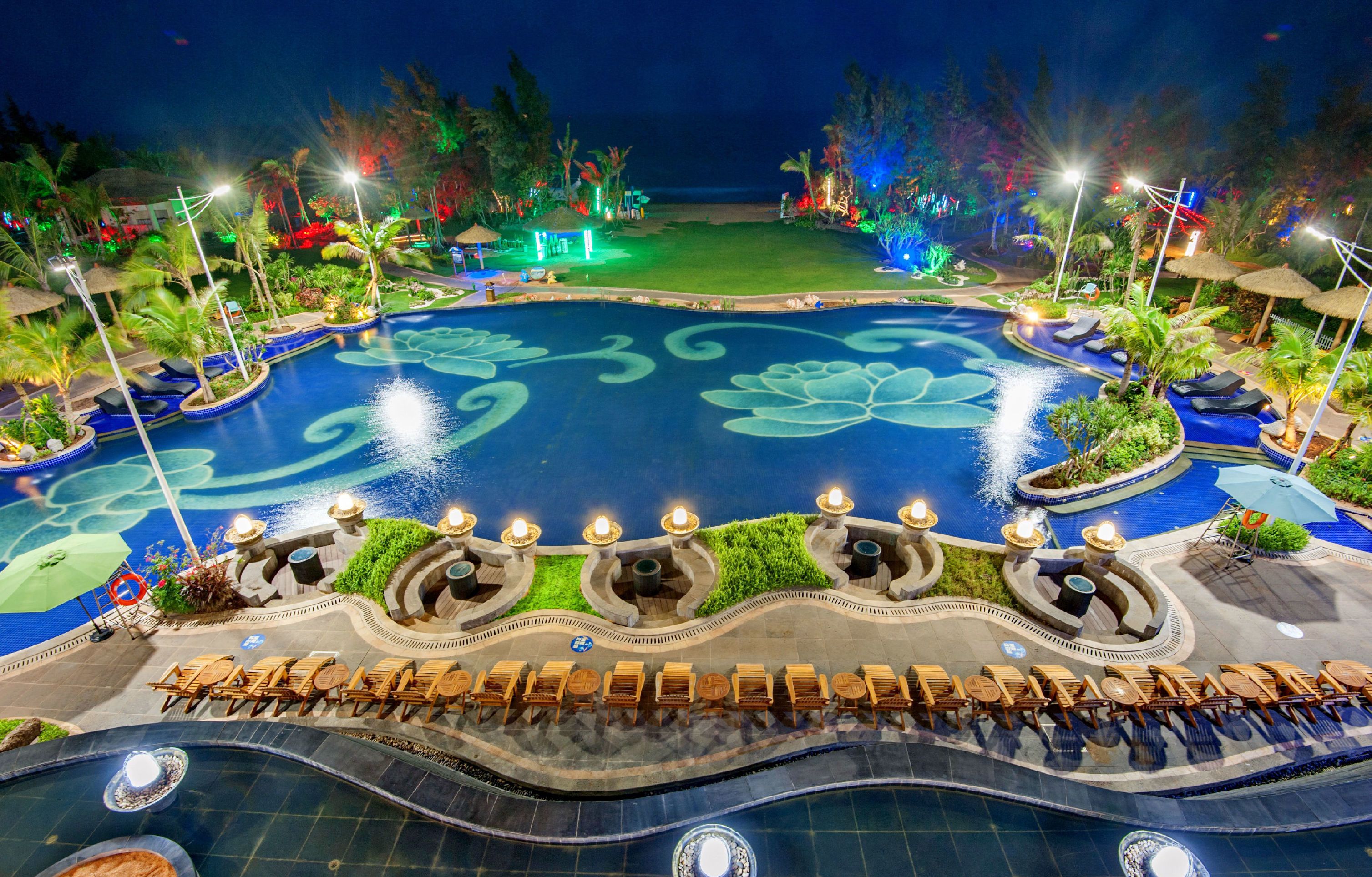 A large, circular pool with a lotus design, surrounded by lounge chairs and palm trees.
