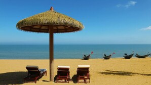 A beach with a thatched umbrella, lounge chairs, and boats in the water. - Country Garden Golden Beach Spring Hotel (Lingao)