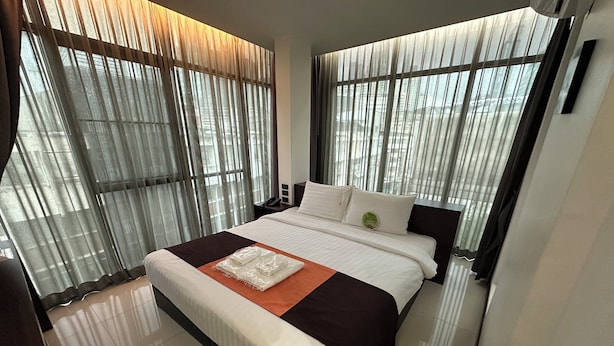 Ein modernes Hotelzimmer mit einem großen Bett, einem Nachttisch und Blick durch leichte Vorhänge.