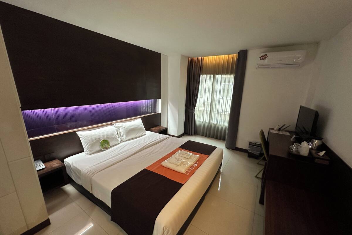 Ein Hotelzimmer mit einem großen Bett, einem Schreibtisch mit Computer und einem Fenster mit Vorhängen.
